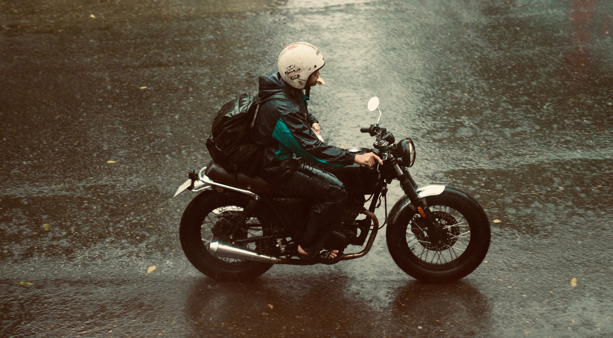Motorcyclist riding in the rain wearing a helmet and weatherproof gear on an urban street