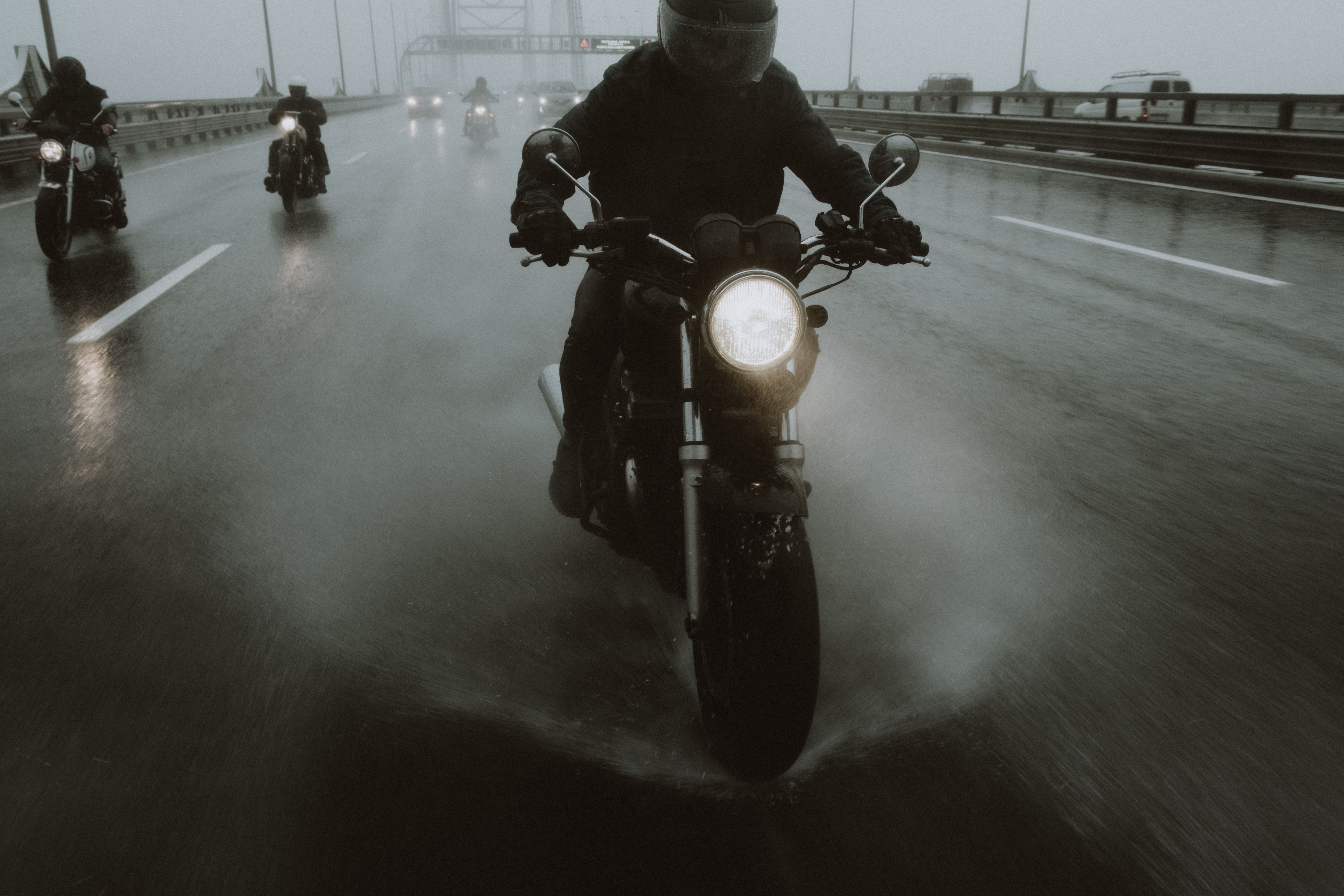 Group of motorcyclists riding in the rain on a wet highway splashing water