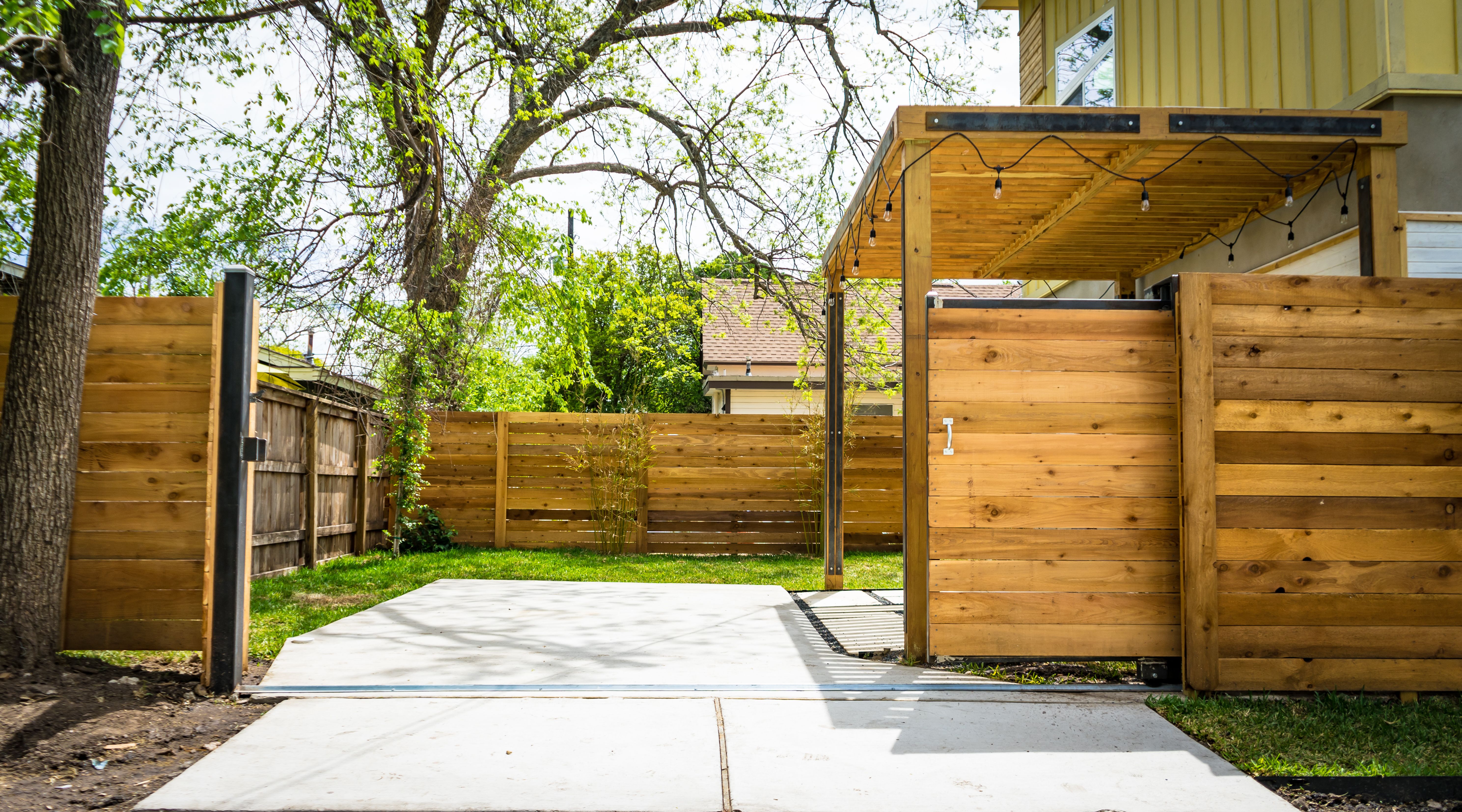 Sunlit fence and garden gate in a residential setting, illustrating a practical privacy barrier beside an access path.