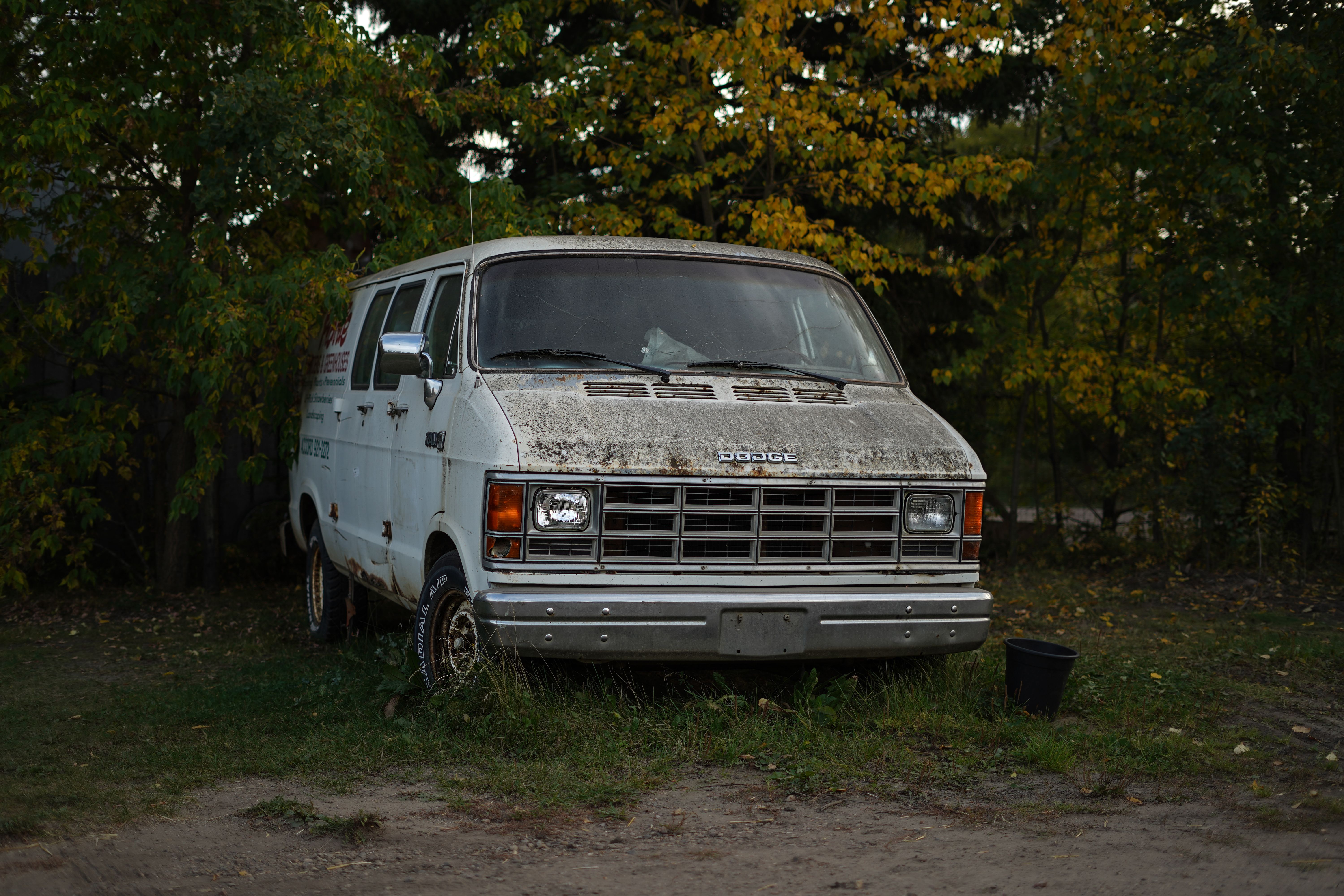 Vintage Dodge van parked among autumn trees, showing the utility-van style that preceded modern family minivans.